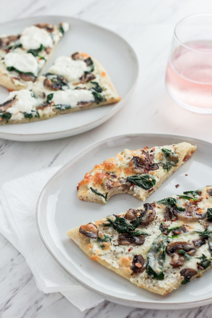 Two plates of mushroom spinach white pizza with a glass of rose in the background
