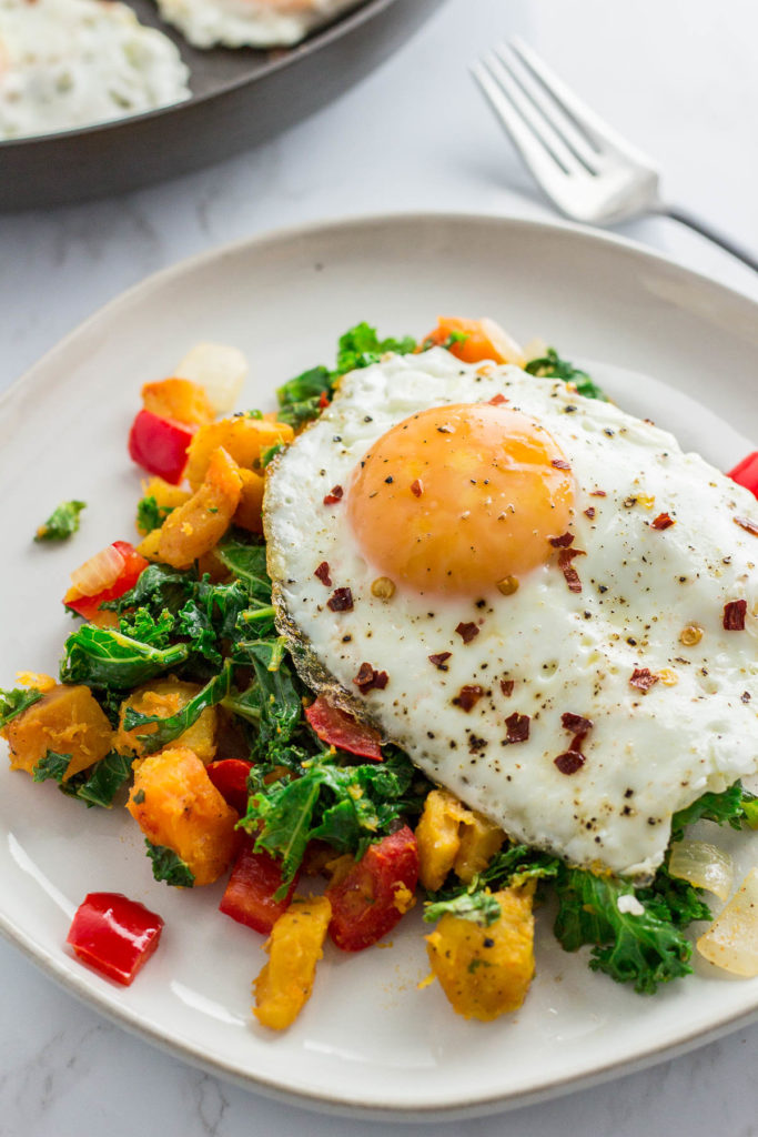 winter squash kale hash on a white plate with fried egg on top