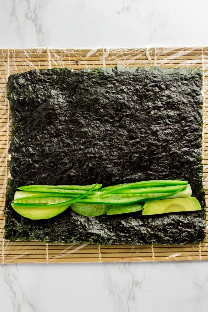 Cucumber, avocado, and jalapeno are added on top of seaweed paper that has been flipped over once the rice was spread on top