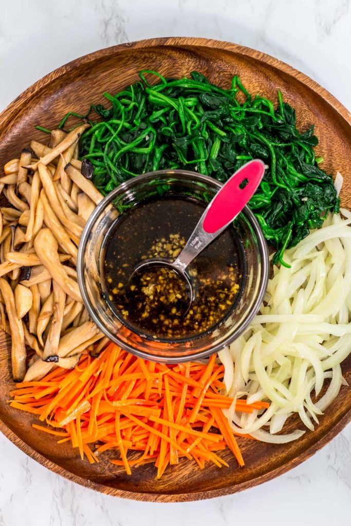 Ingredients to make japchae - blenched spinach, sauteed onion and carrots, and stir fried king oystered mushroom with sauce in the middle