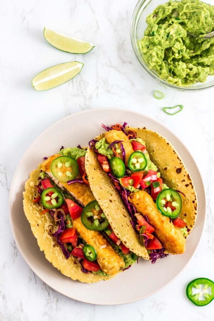 two prepared vegan fish stick tacos on a plate with guacamole in the background