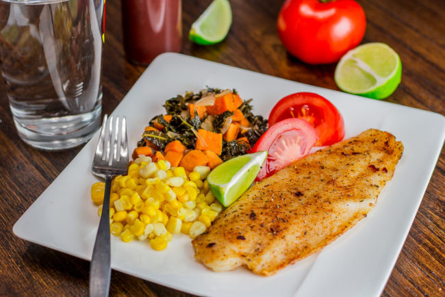 Oven baked swai fish with corn and sweet potato kale hash on a plate with a wedge of lime