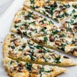 Whole mushroom and spinach white pizza cut up in the baking sheet after baking in the oven