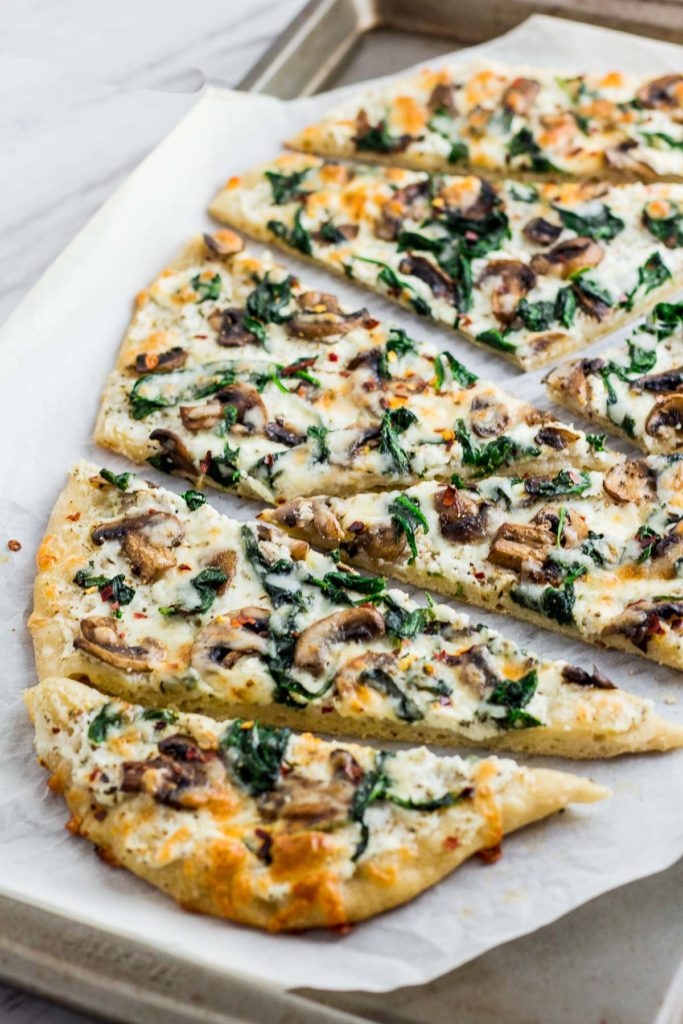 Whole mushroom and spinach white pizza cut up in the baking sheet after baking in the oven