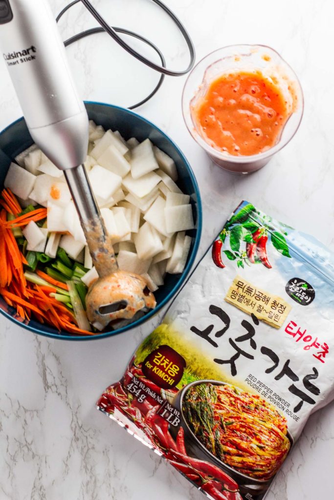 Ground up sauce with prepared vegetables for the kimchi in a bowl and a bag of korean red pepper flakes on the side