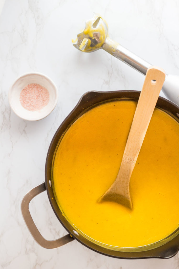 In process of blending soup with the immersion blender. Small bowl of salt next to the pot.