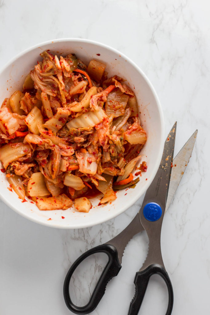 fermented kimchi in a while bowl that has been cut bite sized with scissor