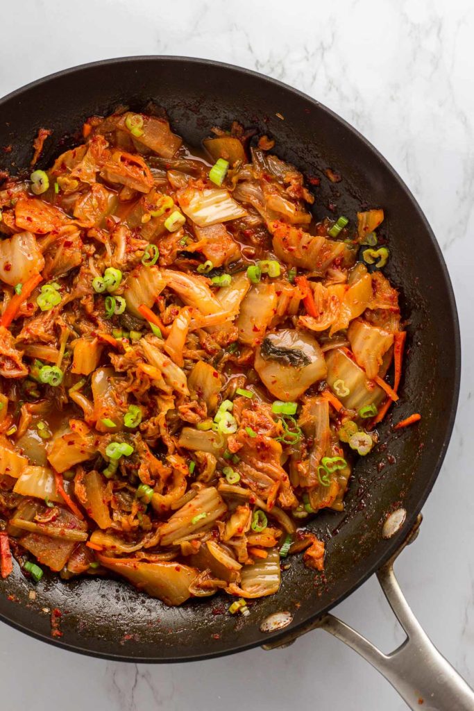 chopped kimchi in frying pan with green onion garnish on top