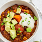 close up shot of bowl of winter squash chili with cashew cream, avocado, and green onion garnish on top