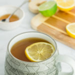 photo of tea with lemon slice on top and have lemon and honey in the background