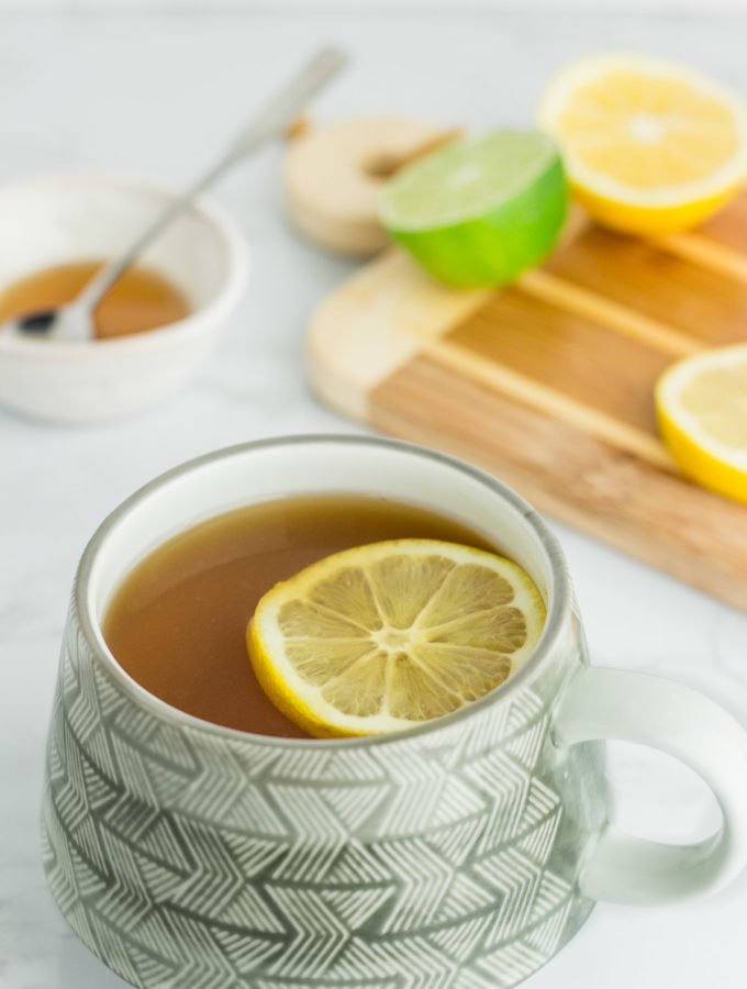 photo of tea with lemon slice on top and have lemon and honey in the background