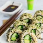 Close up shot of inside out vegan green sushi roll. The rolls are placed on top of rectangular plate with soy sauce in the back ground.