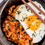 A black bowl full of kimchi fried rice with fried egg on top