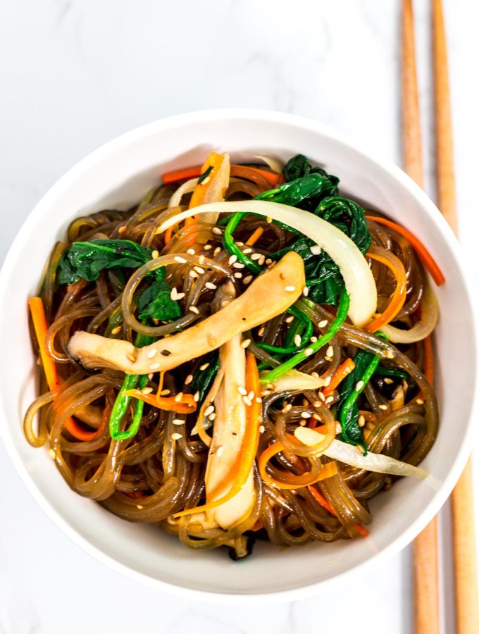 Overhead shot of japchae in a white bowl with chopsticks next to it