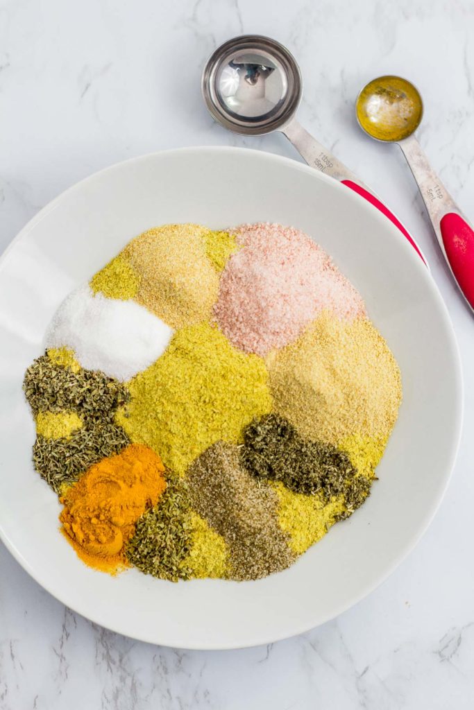 All the ingredients to make the bouillon powder in the white bowl with a tablespoon and a teaspoon in the background