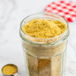 A clear jar full of chicken flavor bouillon powder with teaspoon in front