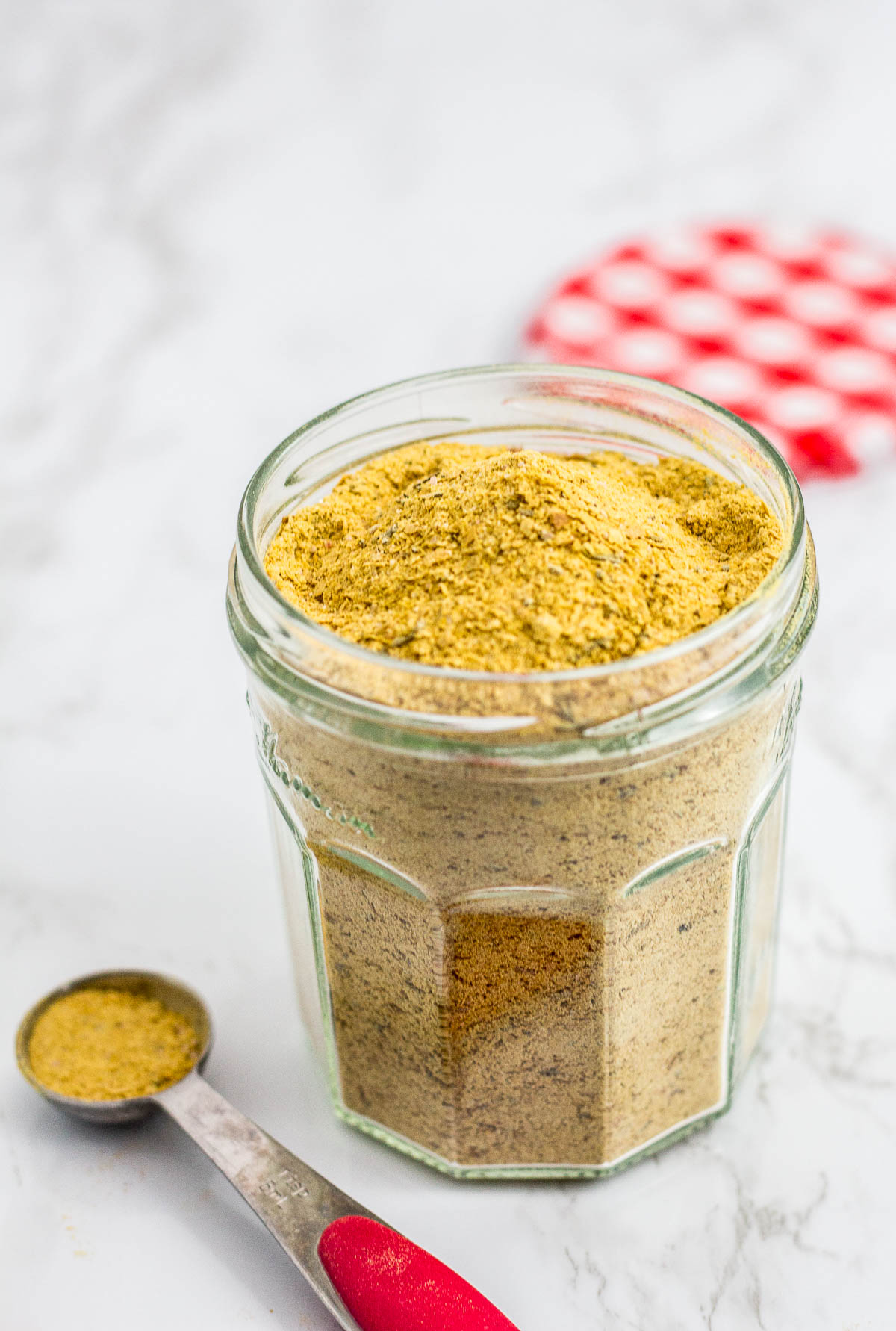 A clear jar full of chicken flavor bouillon powder with teaspoon in front