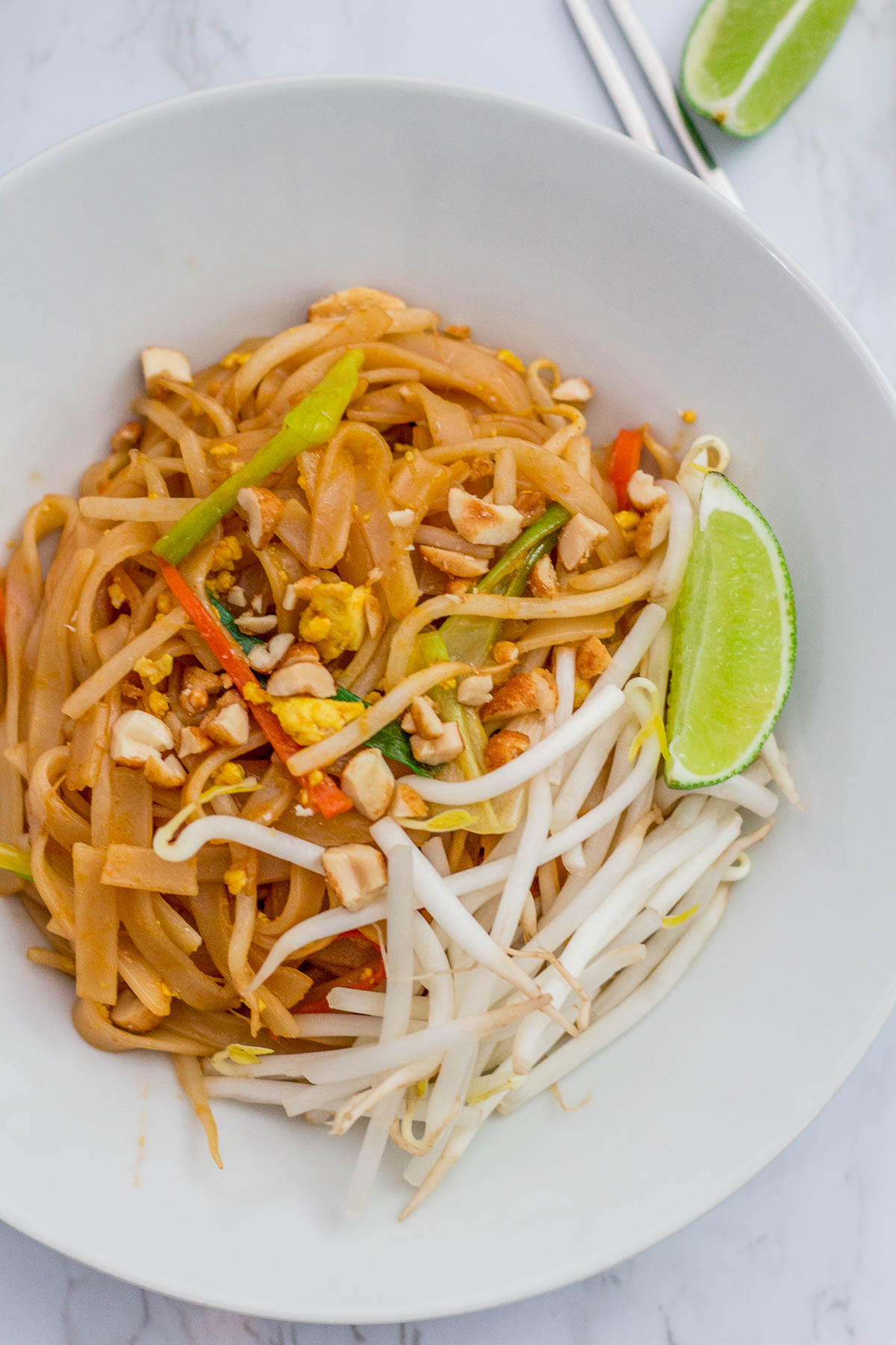 Over head shot of vegan Pad Thai in white bowl with lime and bean sprout garnish