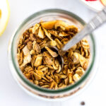 Overhead shot of small batch cashew coconut granola in a clear glass jar with the spoon sticking out