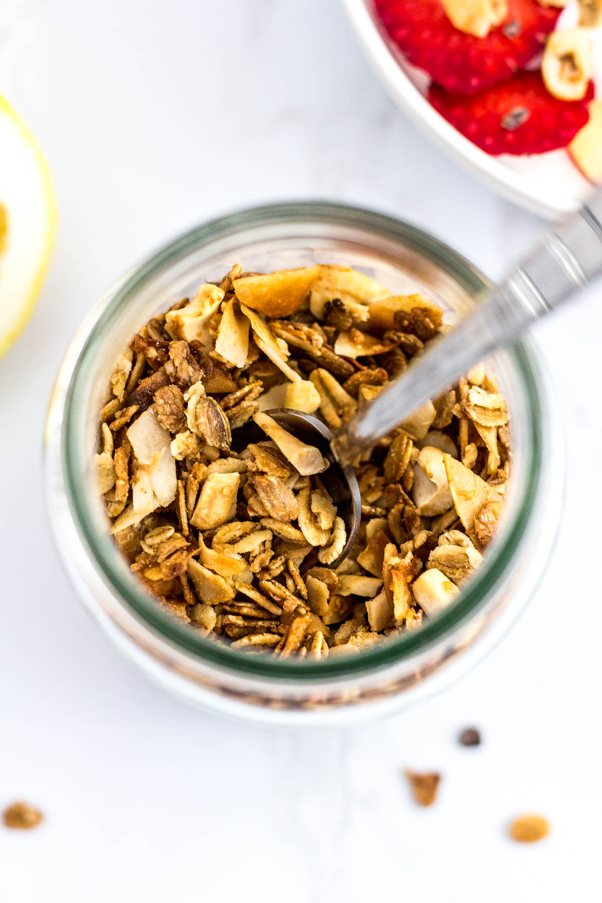 Overhead shot of small batch cashew coconut granola in a clear glass jar with the spoon sticking out