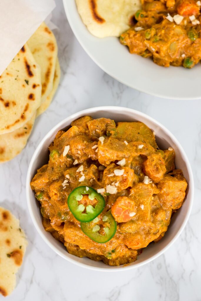 bowl full of Indian style vegan vegetable curry and naan on the side