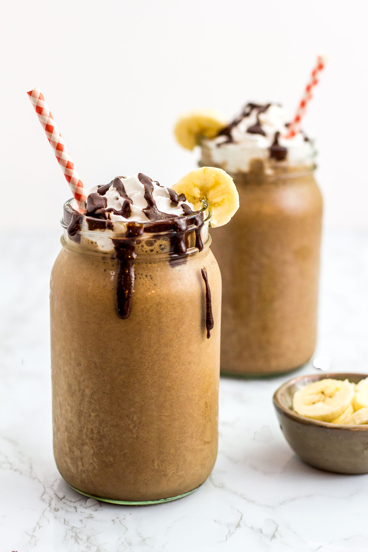 close up shot of mocha flavor banana protein smoothie. Decorated with coconut whip cream, chocolate drizzle, and a banana slice