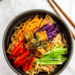 noodle salad in the black bowl with different vegetables and teriyaki tofu on top