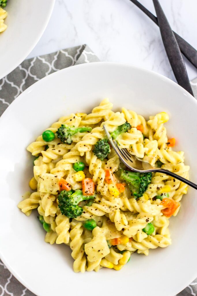 A plate full of no dairy white sauce veggie pasta with gray napkin underneath.