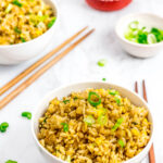 two bowls of super easy 5 ingredients egg fried rice with sriracha and green onion on the side