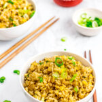 two bowls of super easy 5 ingredients egg fried rice with sriracha and green onion on the side