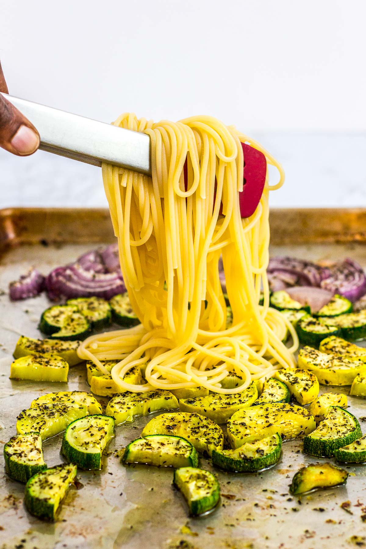 Adding boiled pasta to the sheet pan full of oven roasted summer veggies