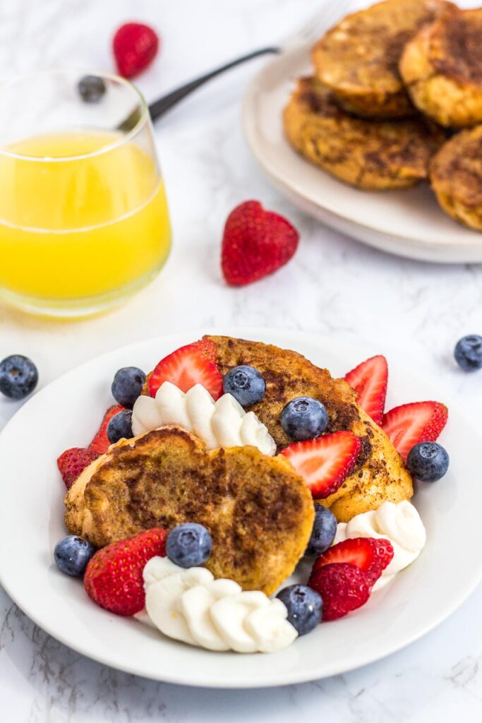 Perfect summer french toast toped with fresh fruits and ricotta and more french toast in the background with orange juice