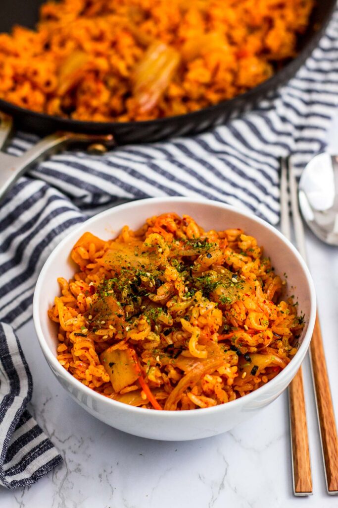 A bowl of vegan kimchi ramen fried rice and more fried rice in the background