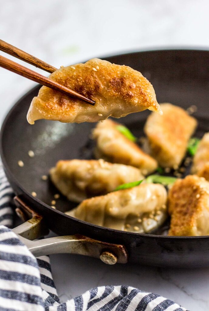 holding a pan fried Homemade Korean Veggie Tofu Mandu/dumpling with chopsticks from a pan