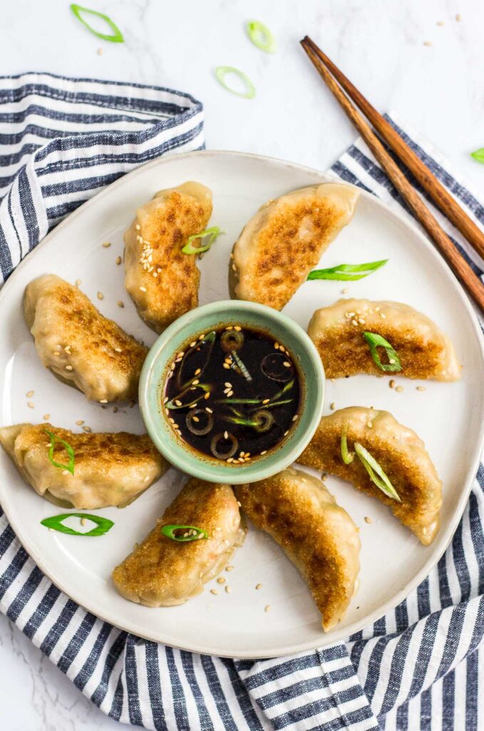 Overhead shot of cooked mandu on a plate with dipping sauce in the middle