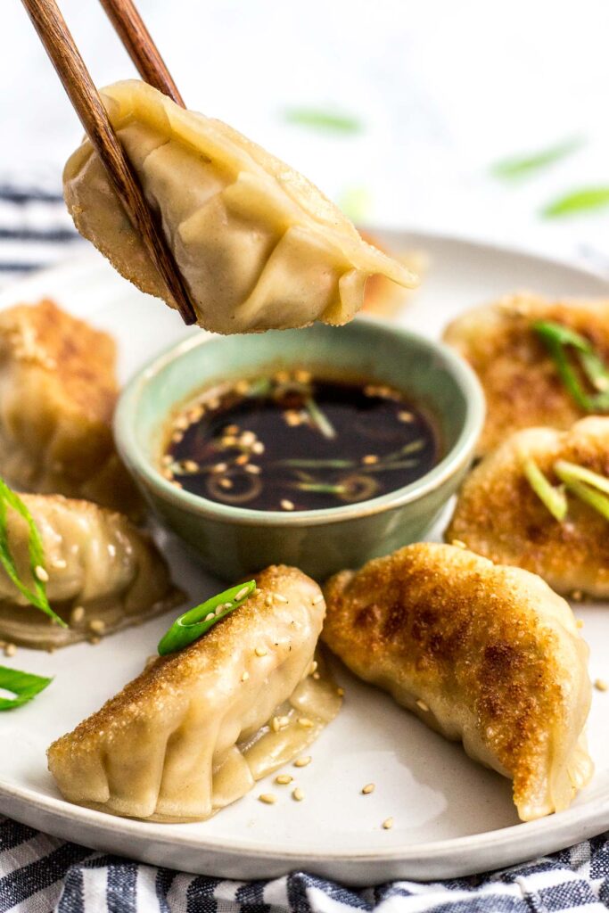 Holding a pan fried Homemade Korean Veggie Tofu Mandu/dumpling with chopsticks from a plate