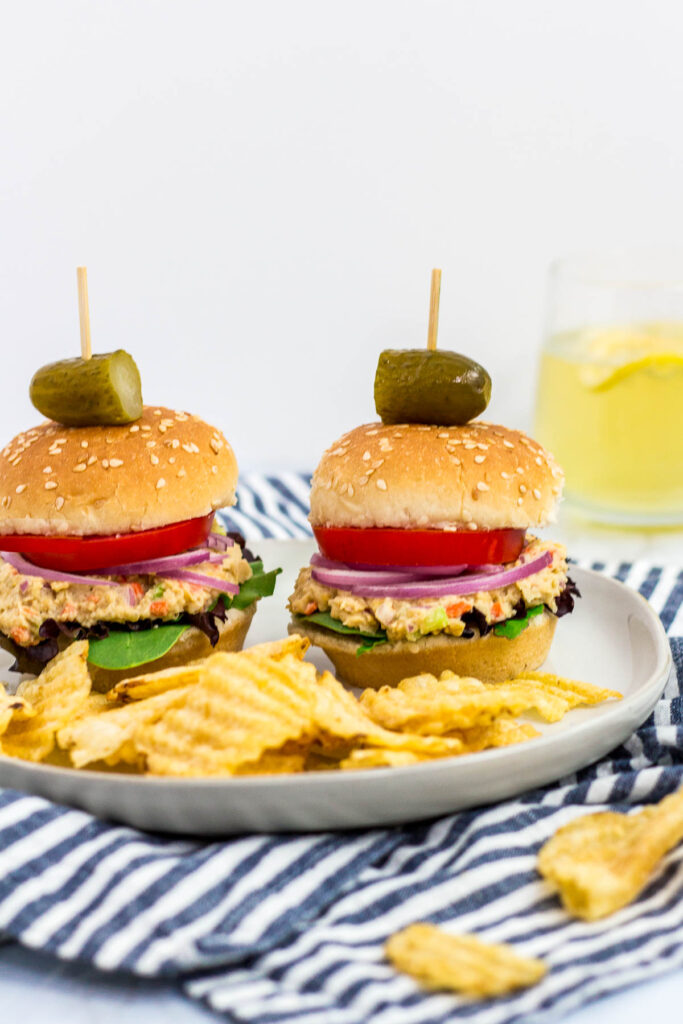 two mini canned chickpea salad sandwiches on a plate with some potato chips and pickles