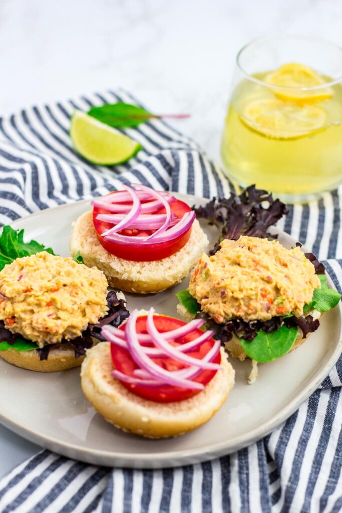 In the making of chickpea salad sandwich - buns, mixed greens, tomato, onion, and chickpea salad