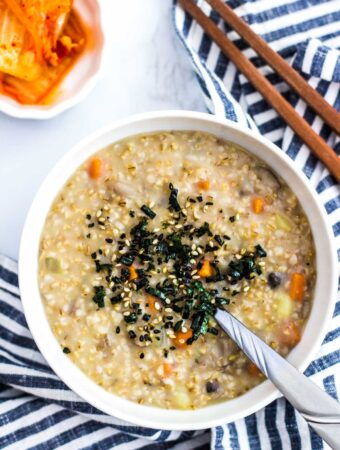 a bowl of savory oatmeal with seaweed flakes topping and side of kimchi