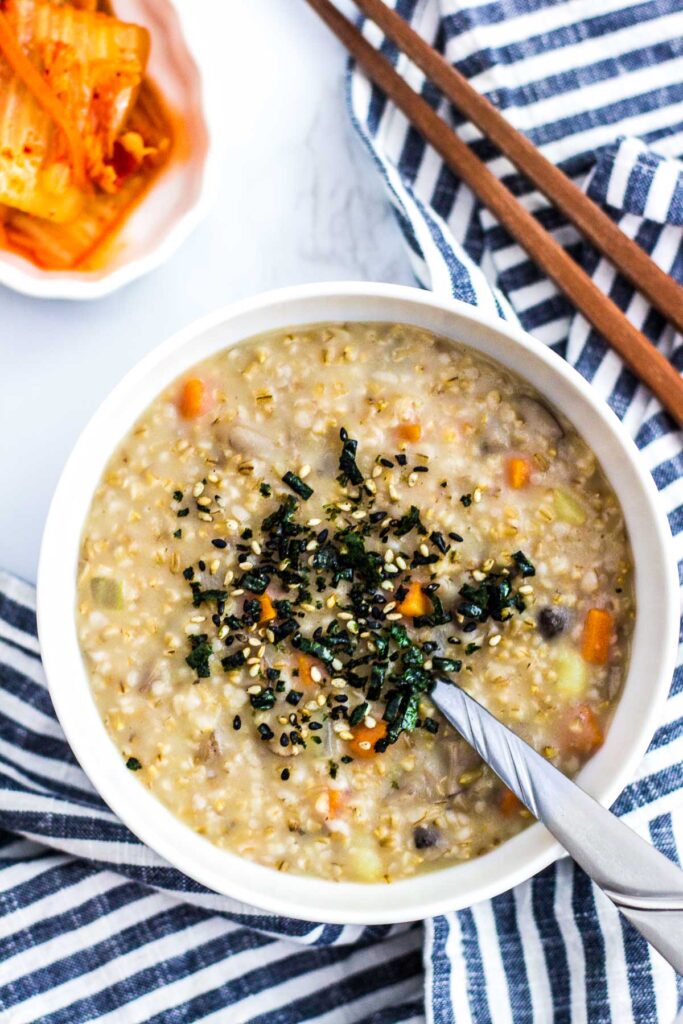 a bowl of savory oatmeal with seaweed flakes topping and side of kimchi