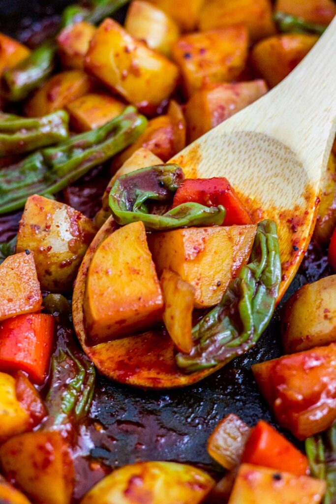 close up photo of spicy braised potatoes and shishito peppers on a wooden spoon