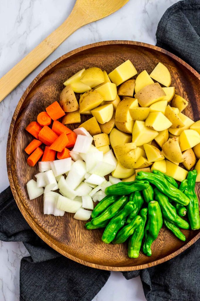 Potato, carrot, onion and shishito peppers on a wooden plate