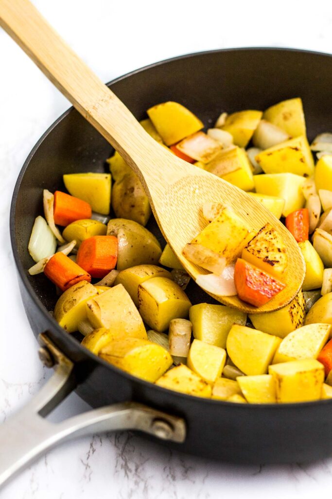 browned potato and carrot pieces with onion in the skillet