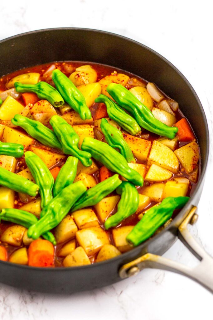 sauce and water is added to browned potato, carrot, onion and shishito pepper in the skillet