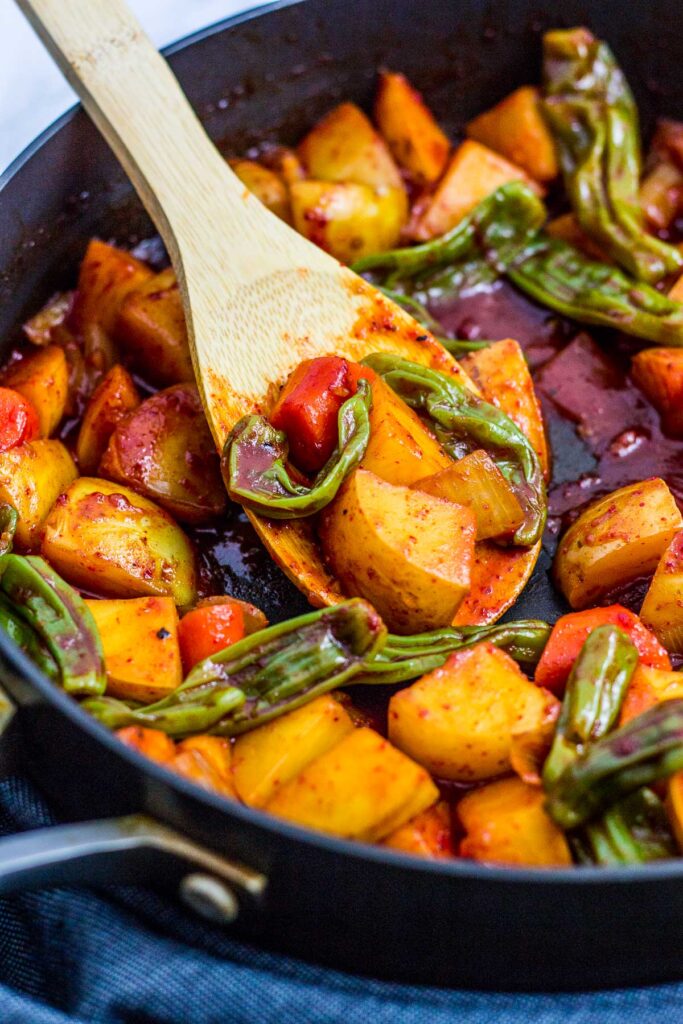 braised potato and shishito peppers in the skillet with a wooden spoon