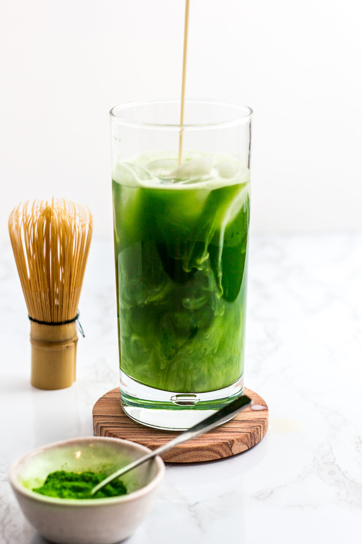 slow pouring of oat milk over iced matcha water