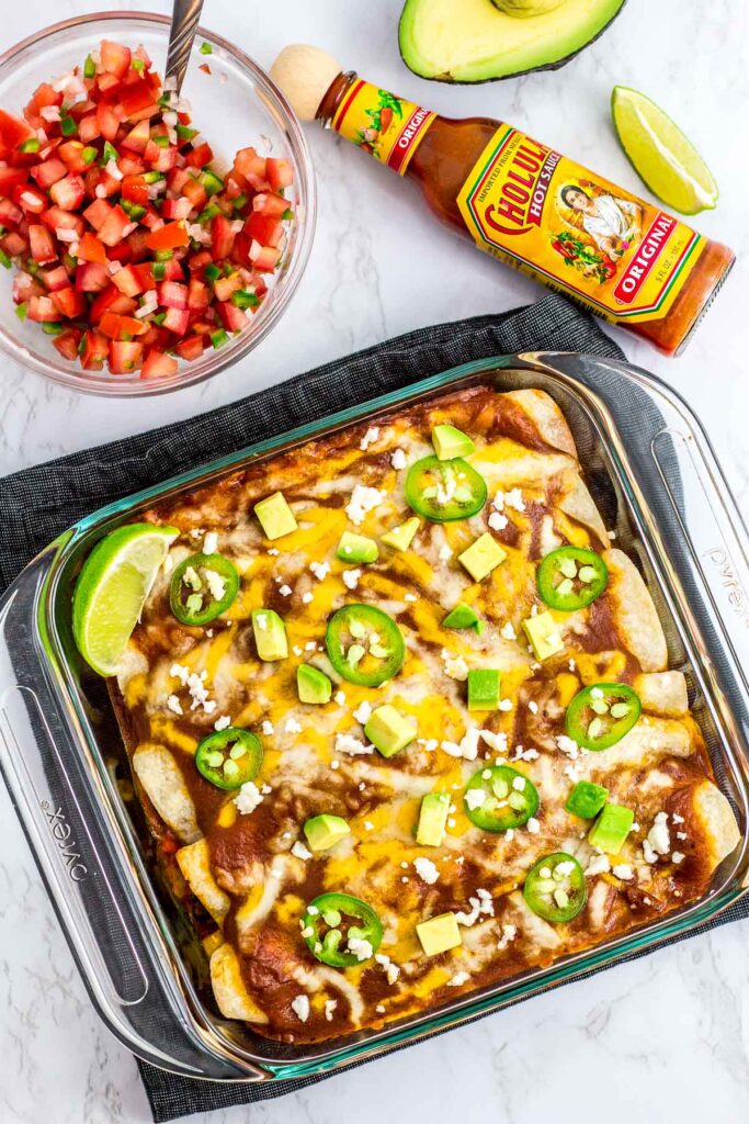 overhead shot of baked vegetarian summer vegetable enchiladas with salsa and hot sauce in the background