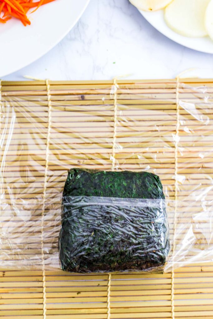 onigirazu being wrapped in a plastic wrap to secure it