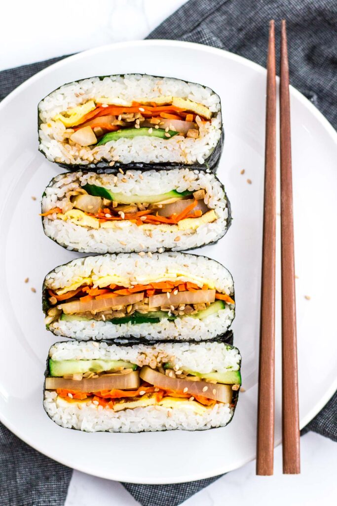 two vegetarian kimbap onigirazu cut in half and placed on a white plate