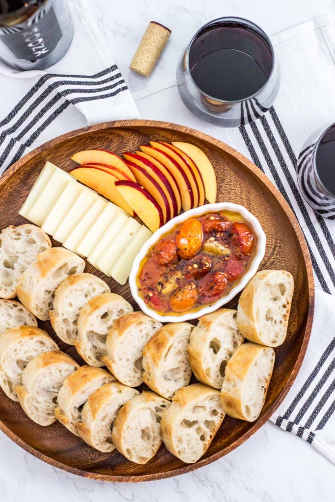 platter of cherry tomato and garlic bread oil with baguette, cheese, and fruit